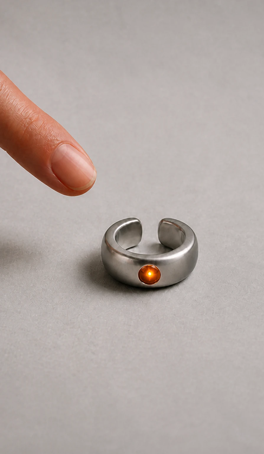 A fingertip pressing the amber sapphire on the Mote Cuff-01 resting on a grey surface